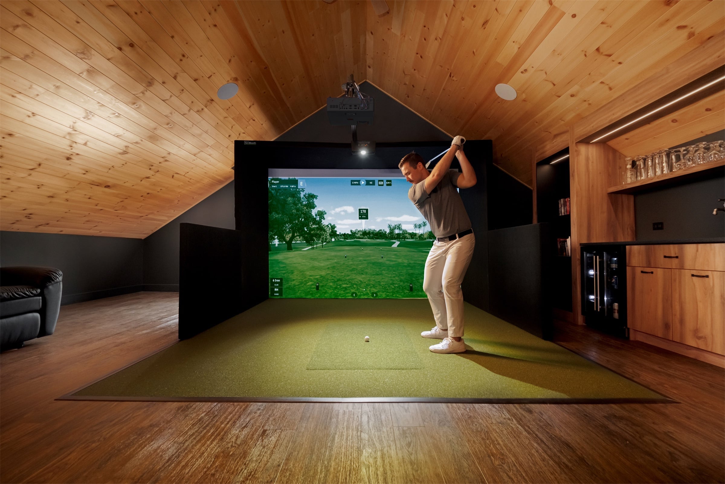 Timber-lined loft simulator bay with player mid-swing
